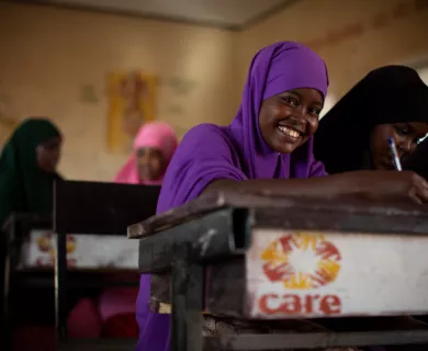 Somalia_Girl in purpule hijab sitting at CARE branded desk smiling at camera